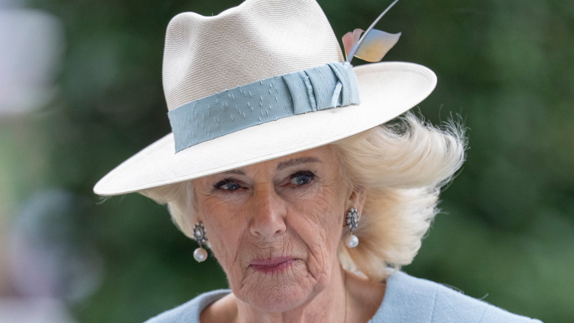 Queen Camilla wearing a fedora with a blue band and pale blue coat