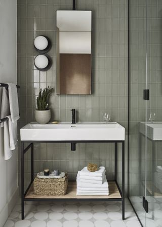 A green bathroom with green wall tiles, a white and black freestanding basin unit, a wall mirror and patterned floor tiles