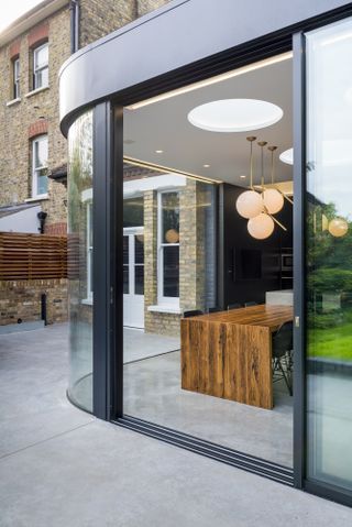an uber-modern kitchen extension by Ar'Chic with floor-to-ceiling doors wrapping around the kitchen, with a wooden dining table