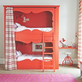 A children's room with a red bunk bed with a striped curtain and a matching desk to the side