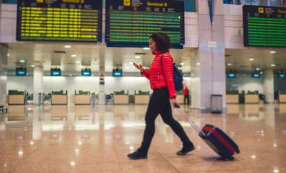 Woman walking through airport with phone and suitcase