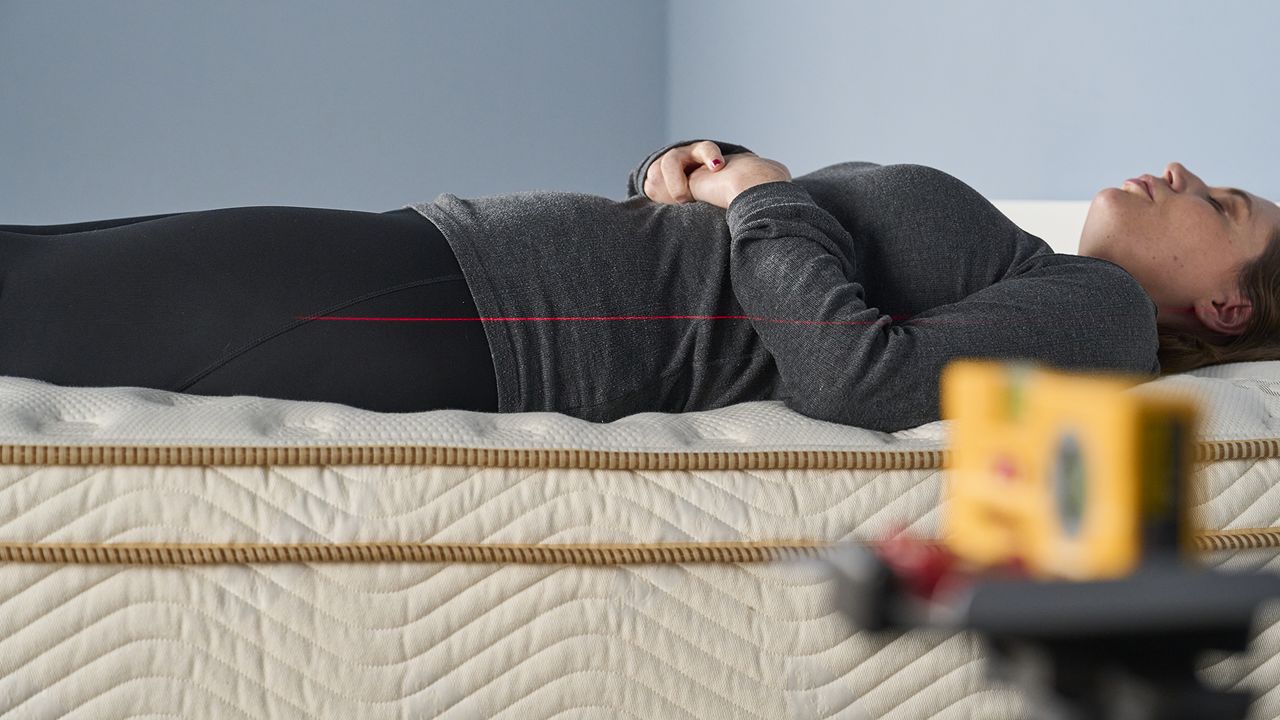 Senior Mattress Staff Writer and Tester Ruth Jones lies on her back on the Saatva classic mattress during our pressure relief Sleep Lab tests. We use a digital laser to project a straight line onto Ruth's body that we can measure against to make sure there is no dipping or sagging around her back. The Saatva Classic keeps her firmly on top of the mattress where her spine is perfectly aligned to prevent pressure points.