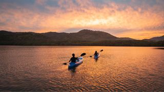 Two women in canoe paddling across a lake at sunset