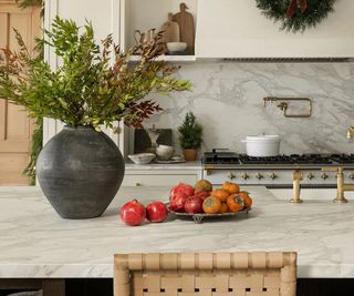 A marble kitchen with a vase filled with branches decorating the island for Christmas