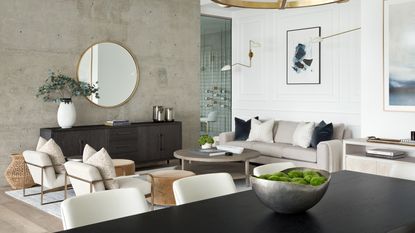 A family room with panelling on white wall, two cream armchairs and a grey sofa, with artwork on the walls