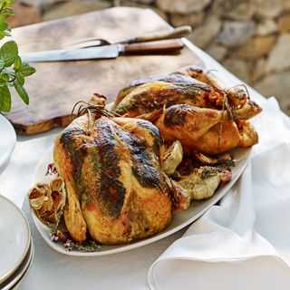 Two roast chickens on decorated table with white table cloth and a wooden carving board set