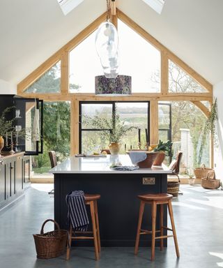 kitchen extension with large oak framed window at end and dark blue island with white worktop in centre