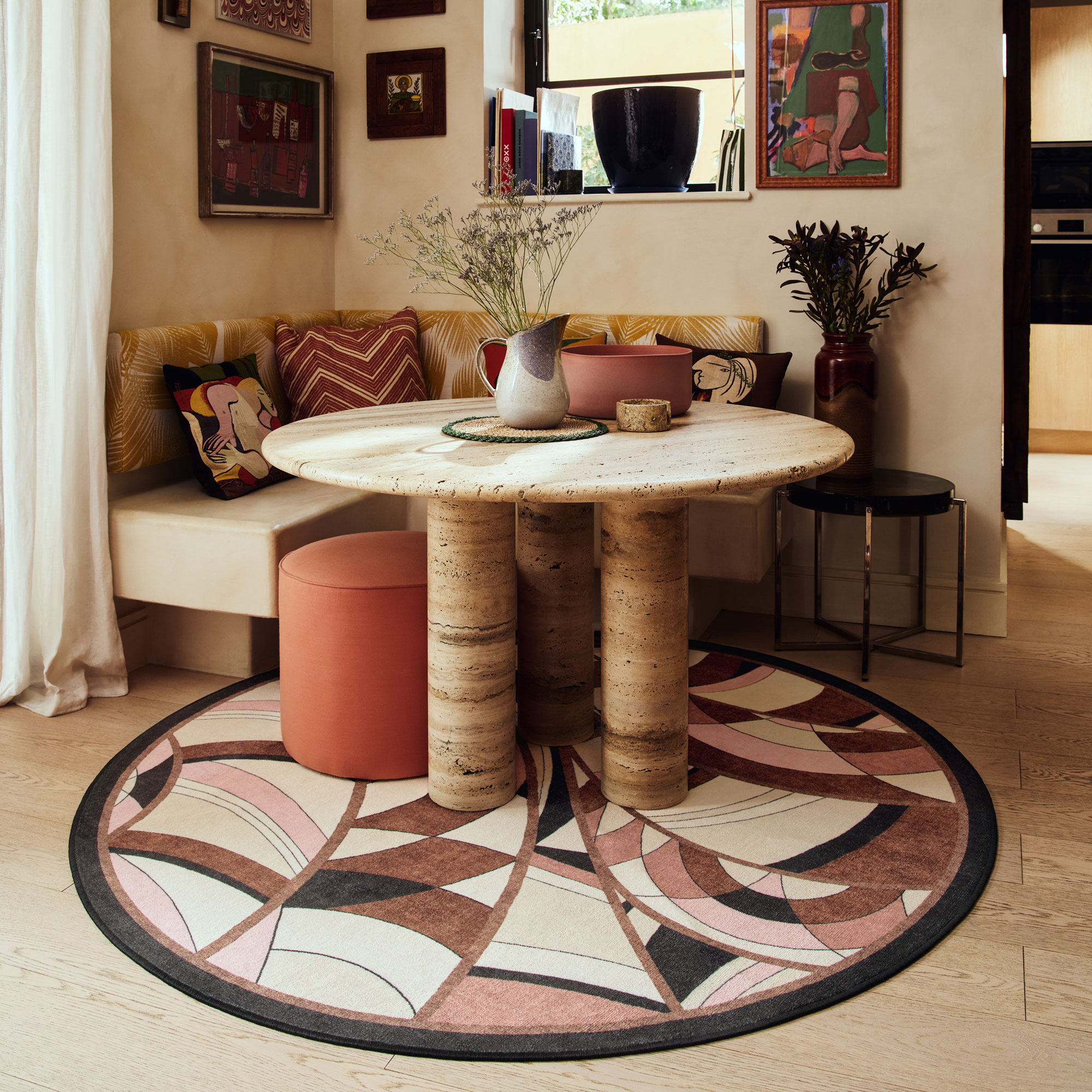 Pink, beige and black art deco style geometric pattern round rug under a round travertine dining table