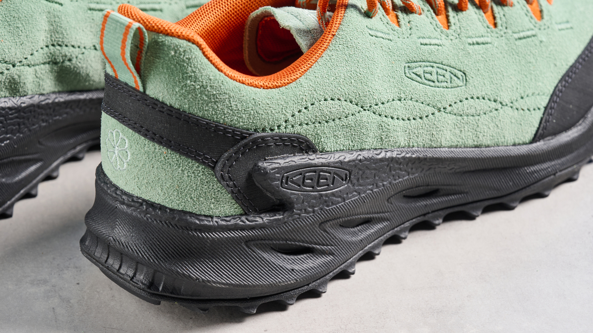 The Keen Jasper Zionic hiking shoes in green/gold colorway are photographed against a blue Tom&#039;s Guide background and a stone floor, showing the lug sole and the leather upper with orange laces