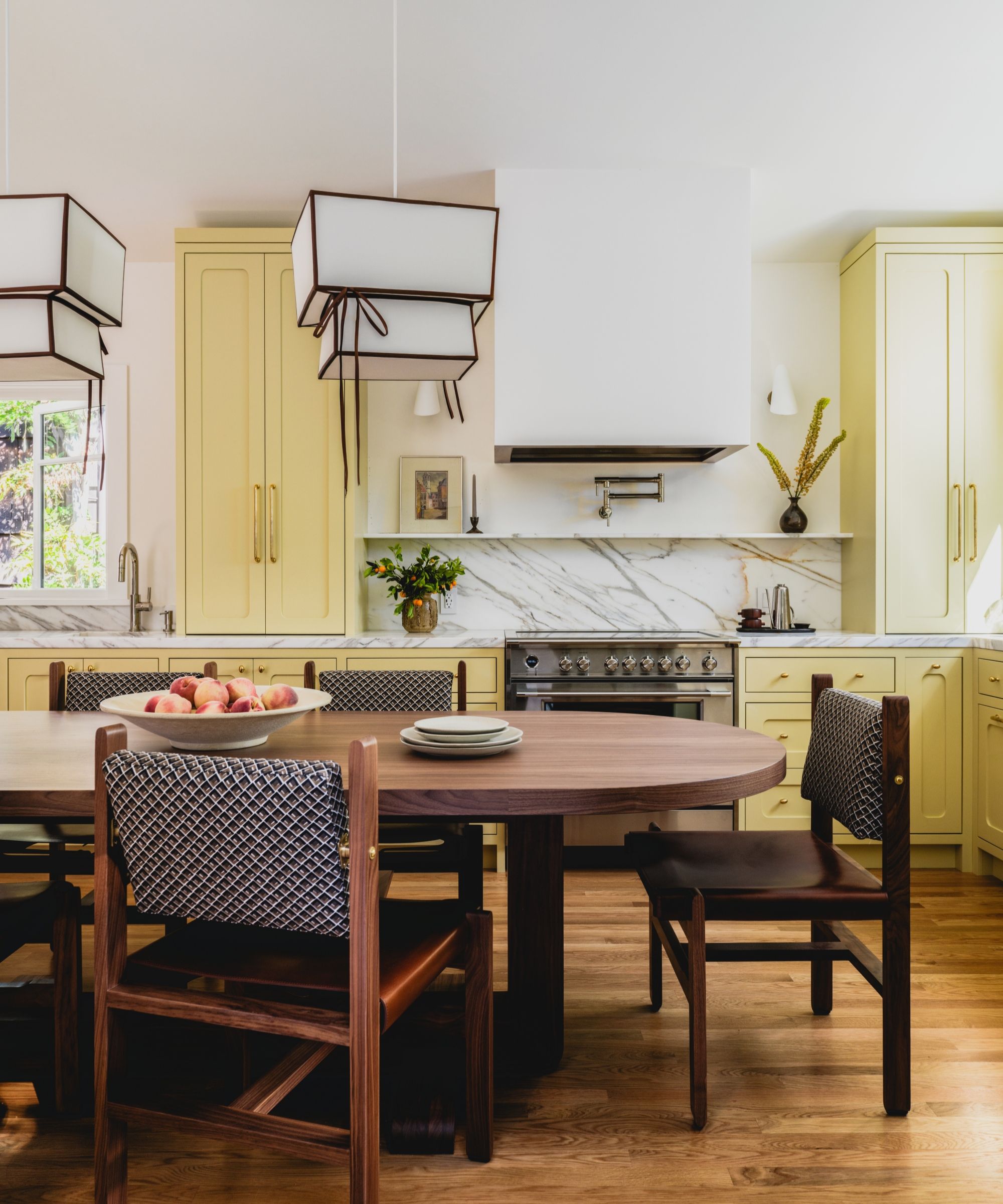 A yellow kitchen with marble countertops, a wooden table, and a stainless steel range cooker