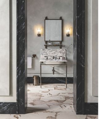 grey marble vanity with metal legs in bathroom with stone floor and grey walls and mirror with sconces