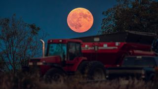 full moon slightly orange color rising over a large harvester machine