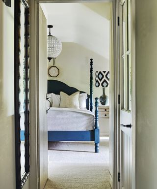 neutral bedroom with blue four poster bed and patterned lampshade