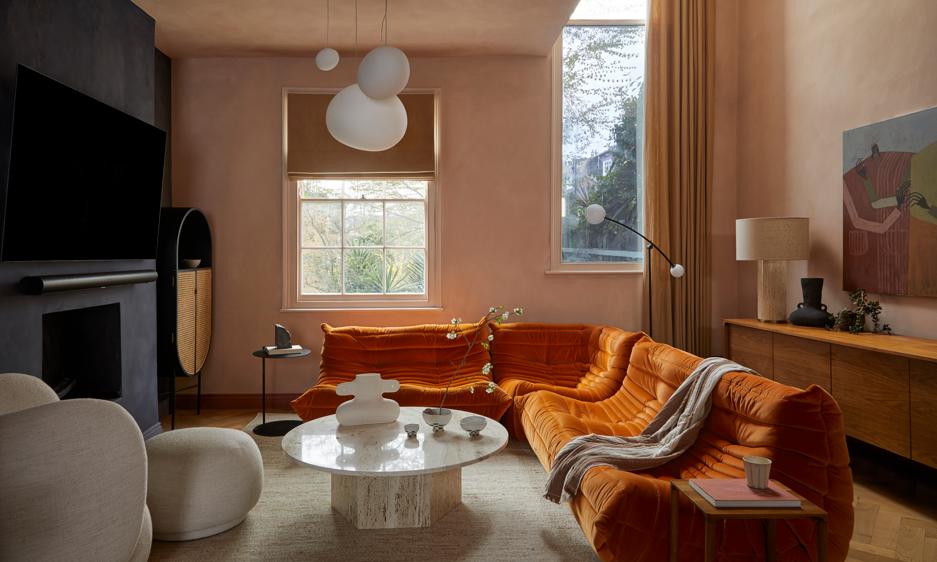 Living room with plaster pink walls, black plaster finish fireplace wall, orange corner sofa, white stone coffee table, beige armchair and white ceiling lights