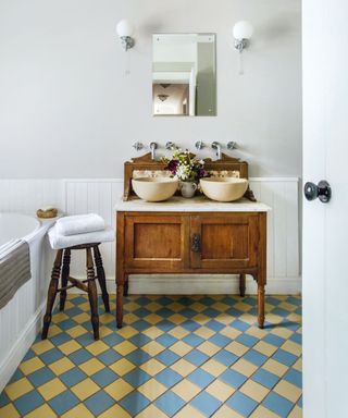 Traditional wooden unit with two round sinks in a bathroom with Victorian floor tiles in blue and yellow.
