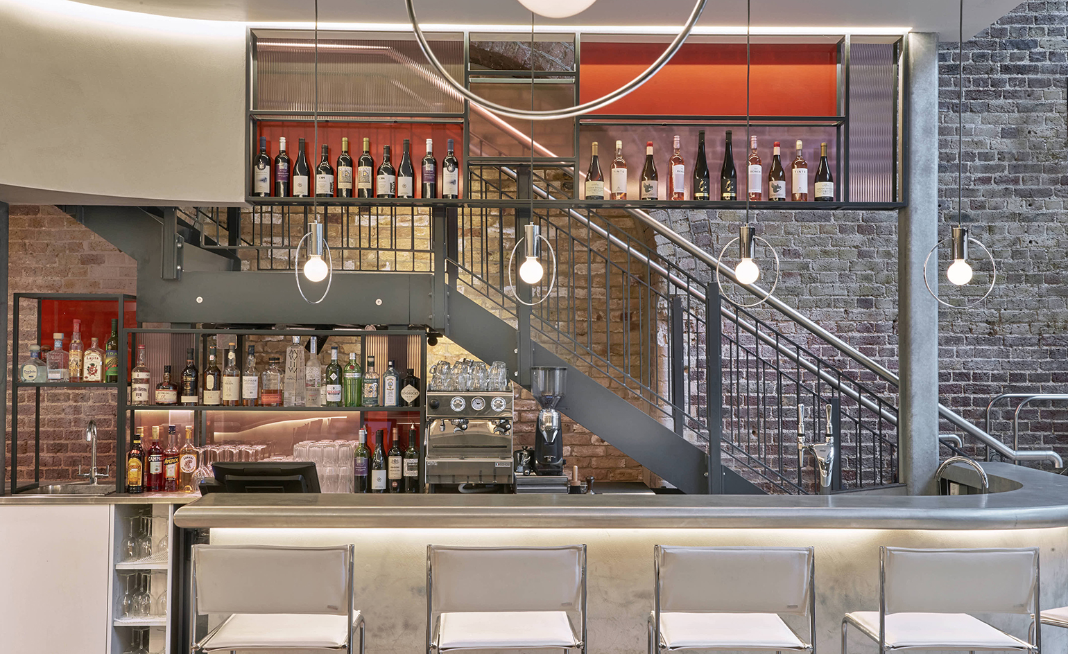 Bala Baya cocktail bar with curved zinc counter, white leather and chrome stools, exposed brick wall and low hanging light bulbs within chrome circles