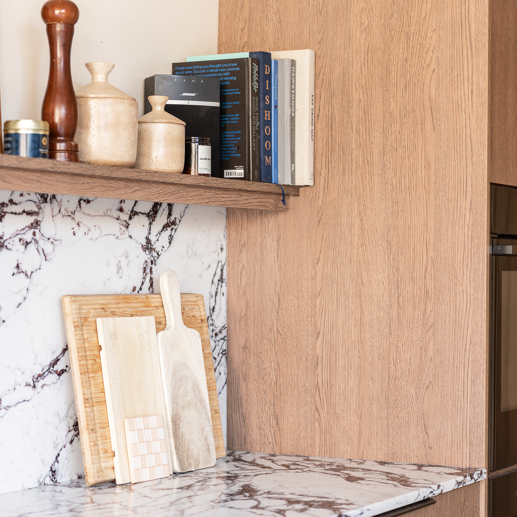 Wooden open shelf running along a wall in a kitchen with marble worktop and splashback