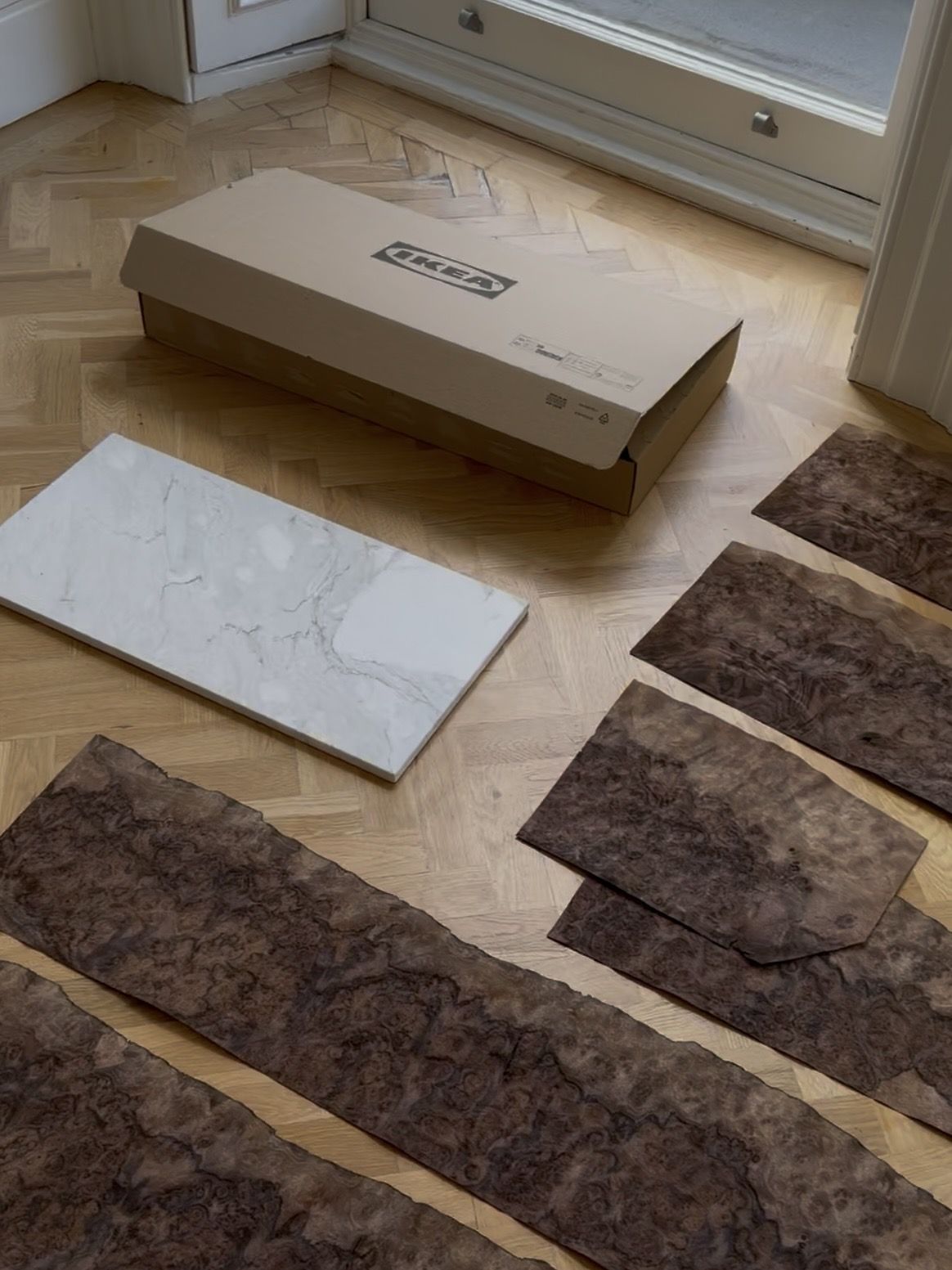 Image of several sheets of burl wood effect panels lying on a hardwood floor with a marble slab and an ikea box next to it.