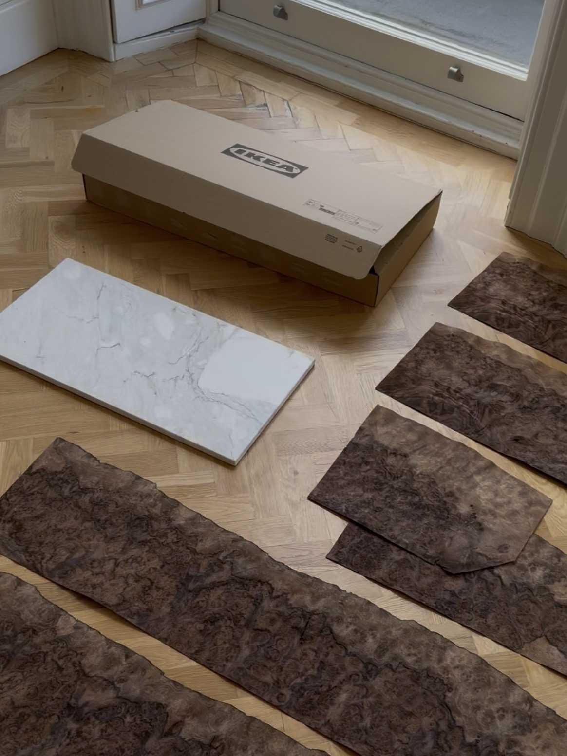 Image of several sheets of burl wood effect panels lying on a hardwood floor with a marble slab and an ikea box next to it.