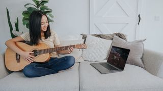 Woman plays acoustic guitar on a sofa