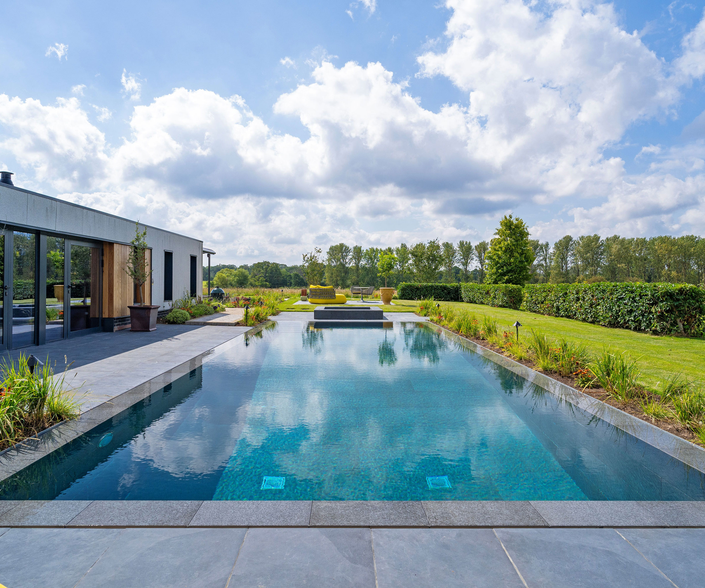 swimming pool and hot tub with patio paving and planting, a screening hedge for privacy and a modern pool house