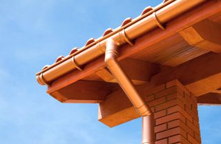 A copper coloured downspout and gutter on a brick house