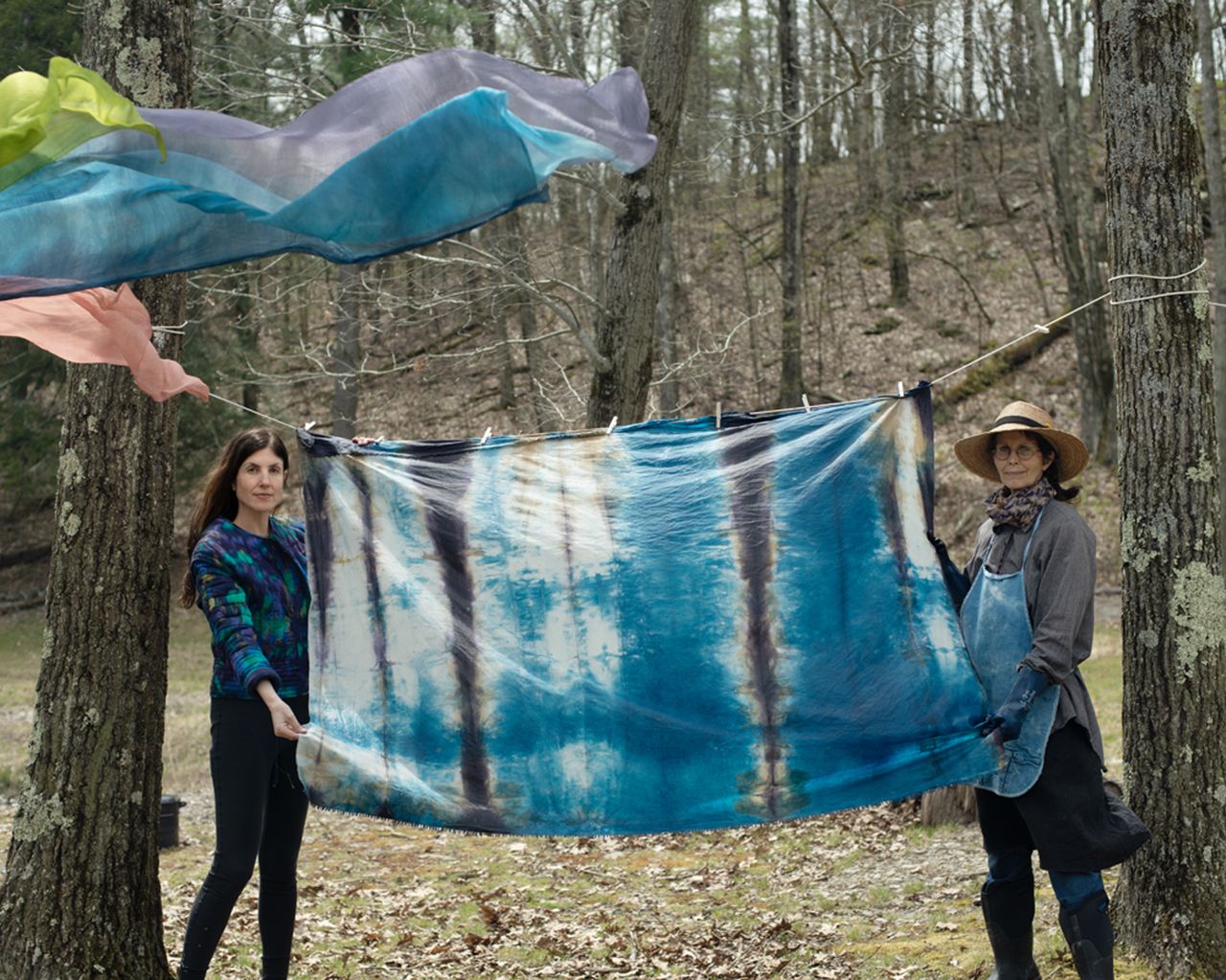 A photo of Rachel Cope and Janene Ping holding up a dyed silk in the wilderness