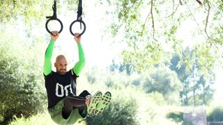 Man hanging from gym rings using arms.