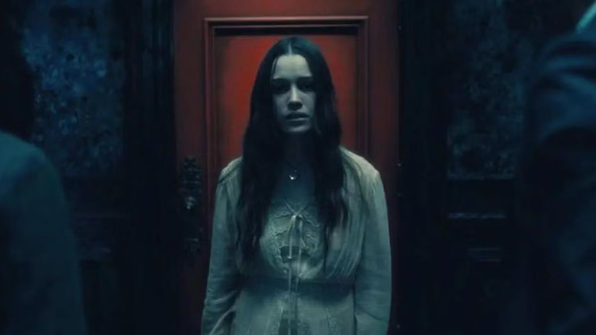 The ghost of a young woman standing in front of a red door during the Netflix horror series, The Haunting of Hill House. 