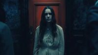 The ghost of a young woman standing in front of a red door during the Netflix horror series, The Haunting of Hill House. 