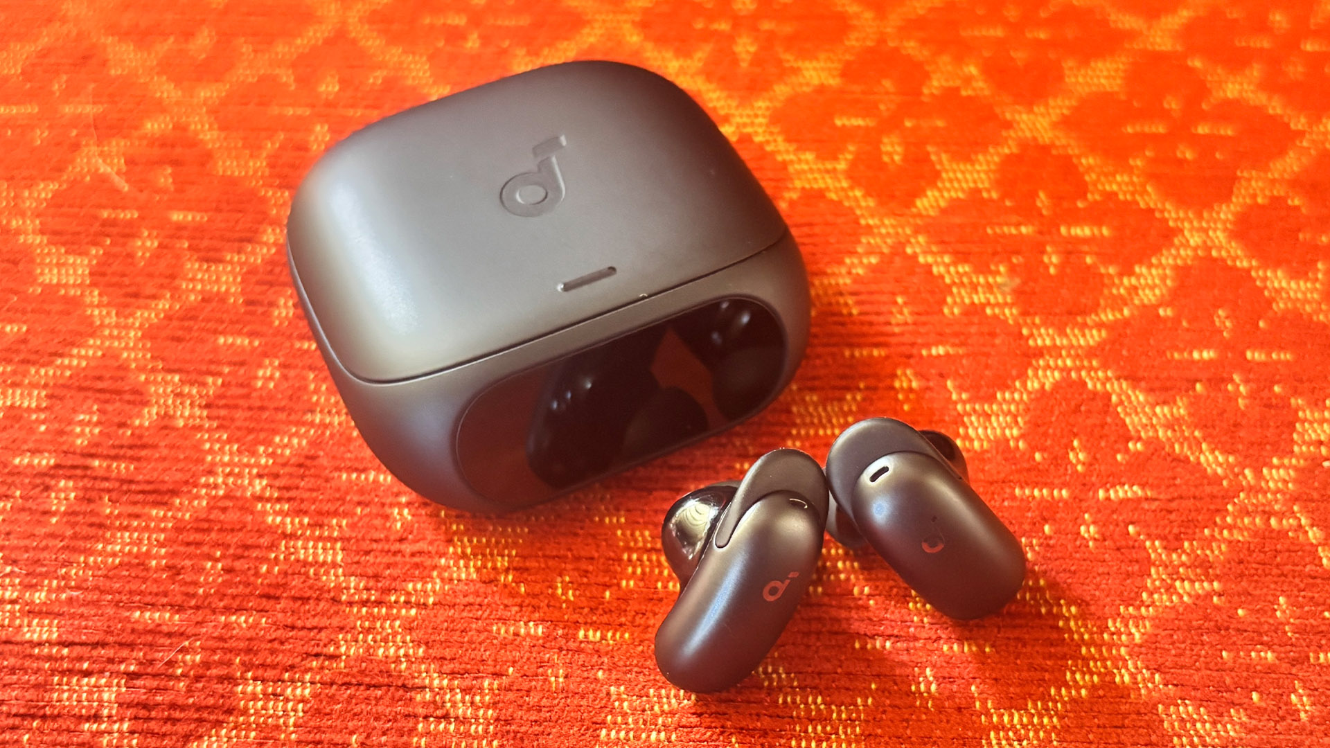 Soundcore Liberty 5 Pro in-ear headphones next to case on red and yellow patterned fabric
