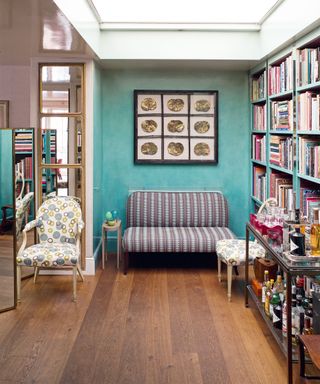 Spacious hallway space with blue painted walls, floor to ceiling bookshelf, upholstered sofa and occasional chair, dark wood flooring, large skylight window