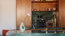 Image of a kitchen with a breakfast nook and wooden cabinetry. There is a large kitchen island covered in teal marble and a coffee machine on the counter.