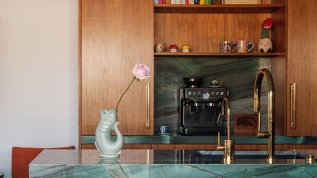 Image of a kitchen with a breakfast nook and wooden cabinetry. There is a large kitchen island covered in teal marble and a coffee machine on the counter.