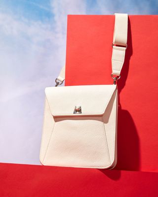 White Akris ‘Anouk Messenger’ bag in front of a red background