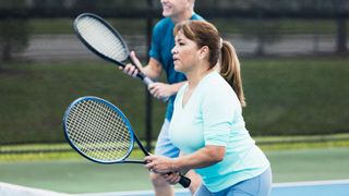 Woman playing tennis on court in fitness kit with male tennis partner next to her