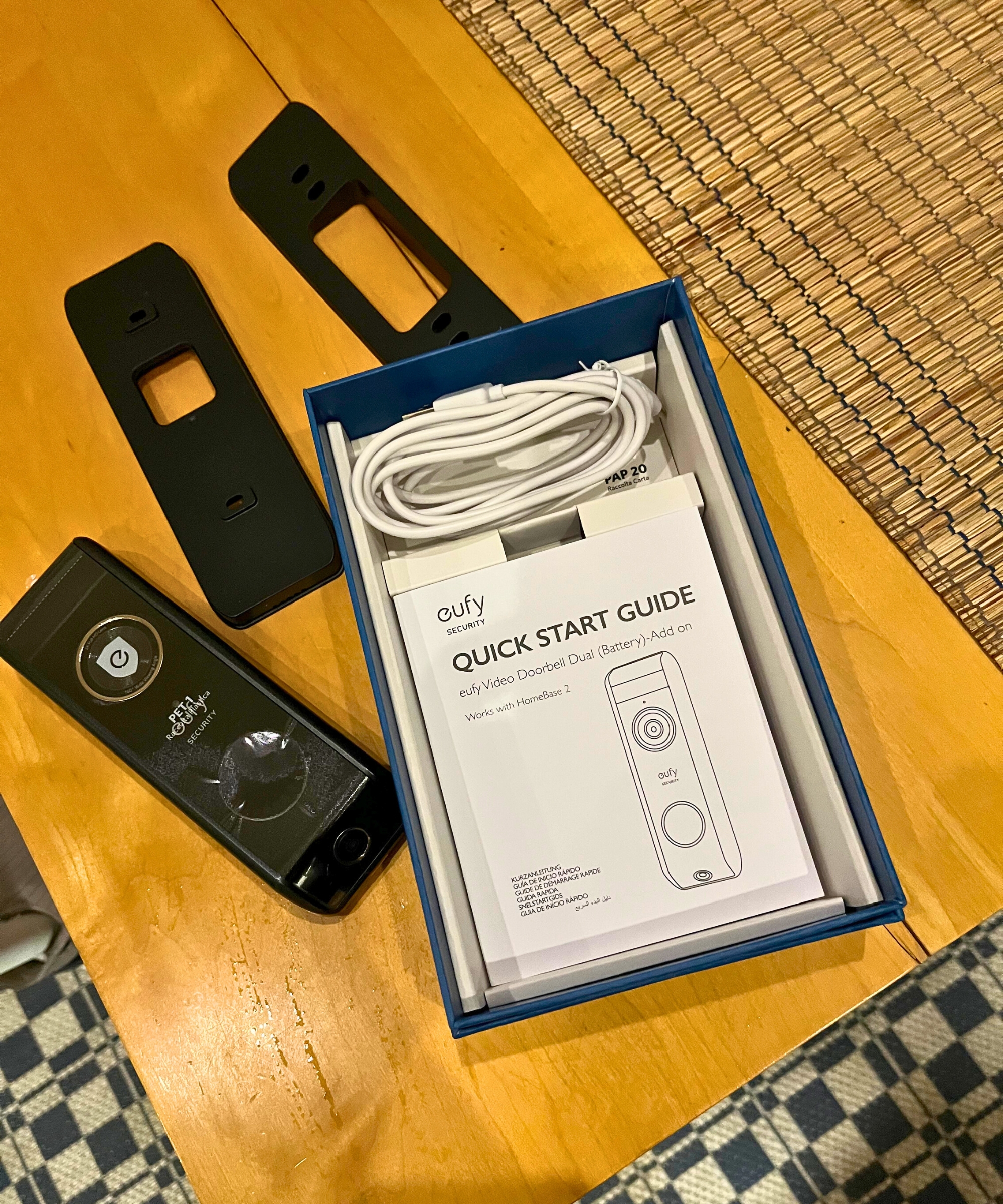 The parts of the eufy S330 video doorbell out of the box on wooden table, above black-and-white checked flooring.