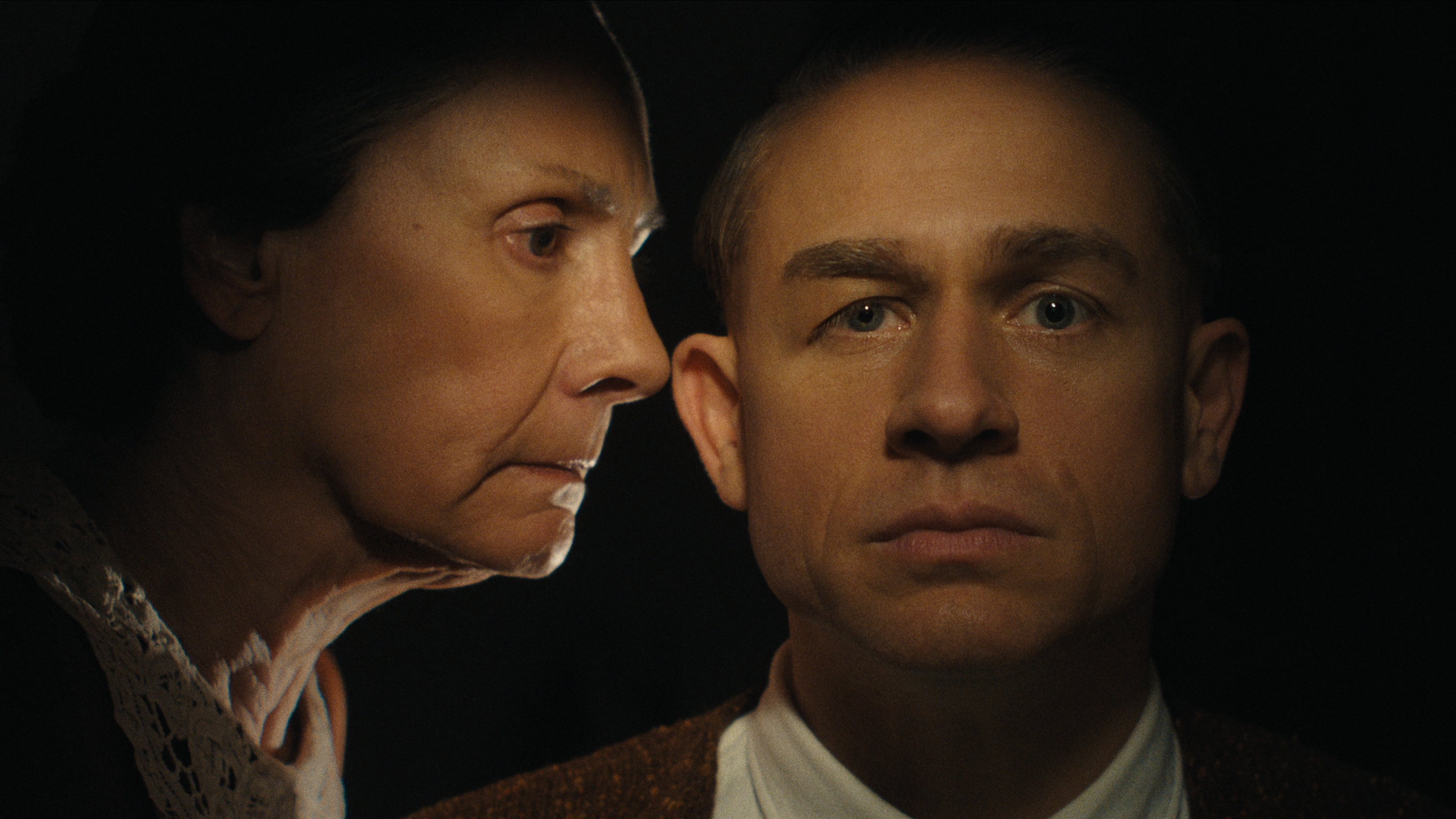 Promotional shot for Monster: The Ed Gein Story. Laurie Metcalf as Augusta Gein gives her son Ed Gein (Charlie Hunnam) a disapproving look as Ed looks directly at the camera against a black background.