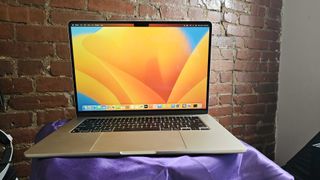 MacBook Air 15-inch open with the display on facing you on a purple tablecloth covered side table in front of a brick wall