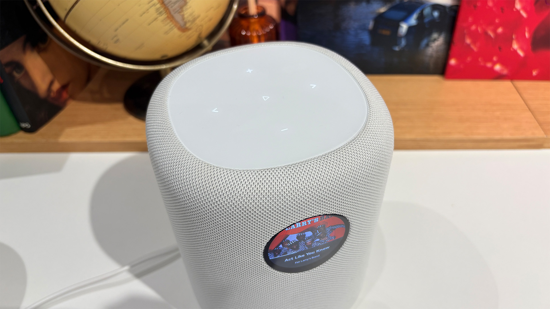 WiiM Sound wireless speaker in white on white surface in front of busy bookshelf