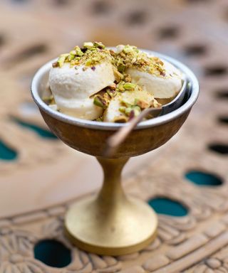 A goblet of cardamom and rose flavored kulfi, topped with pistachios