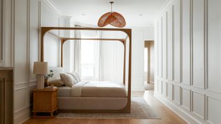 A blonde wooden four poster bed in the center of a large primary bedroom