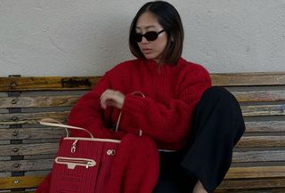 Woman wearing a red sweater reaching into a red Louis Vuitton bag.