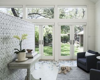 An example of patio door ideas showing traditional white patio doors in front of a tiled monochrome wall and black armchair