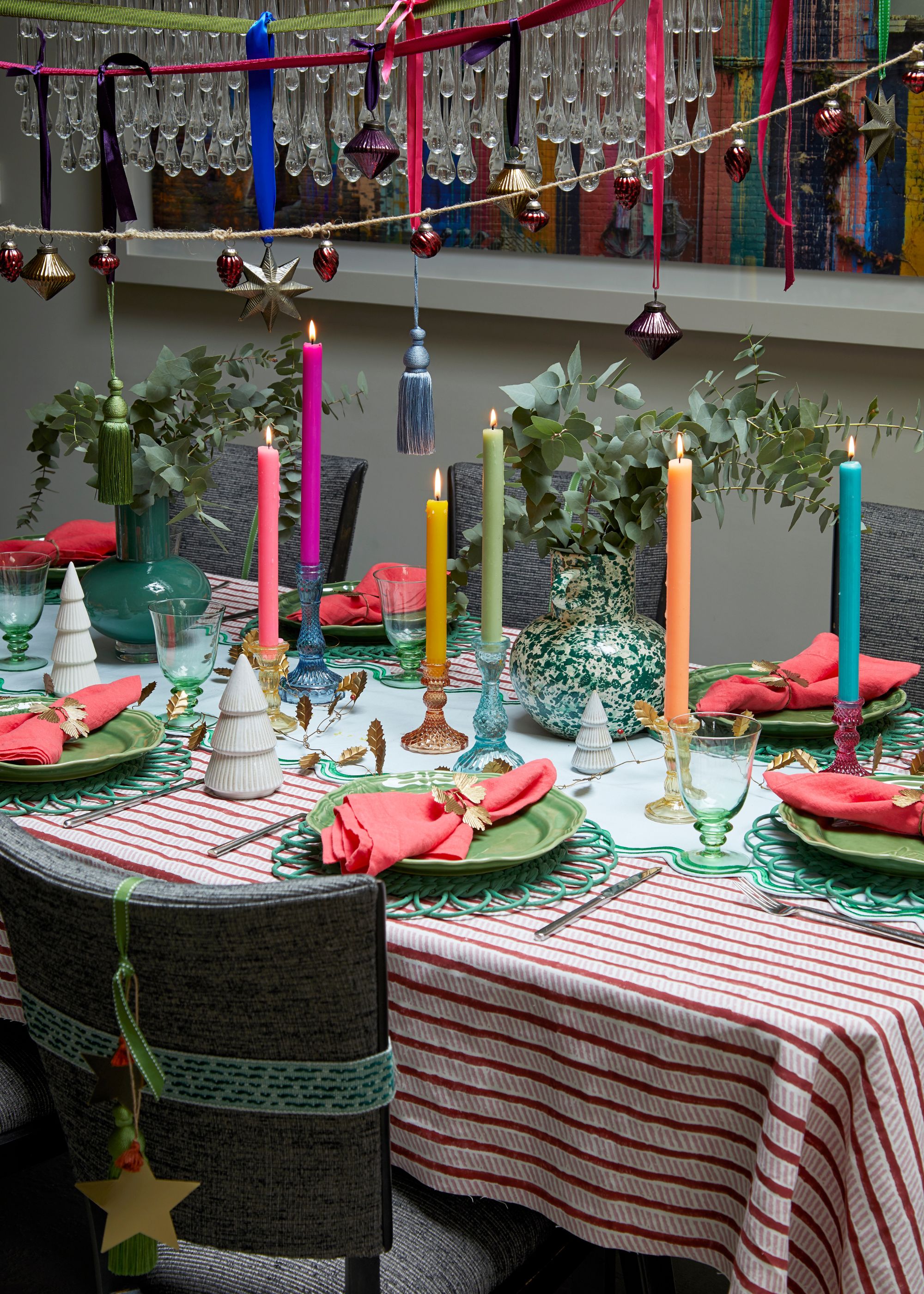 A festive tablescape with a red and white striped tablecloth, colorful taper candles, and foliage in vases.