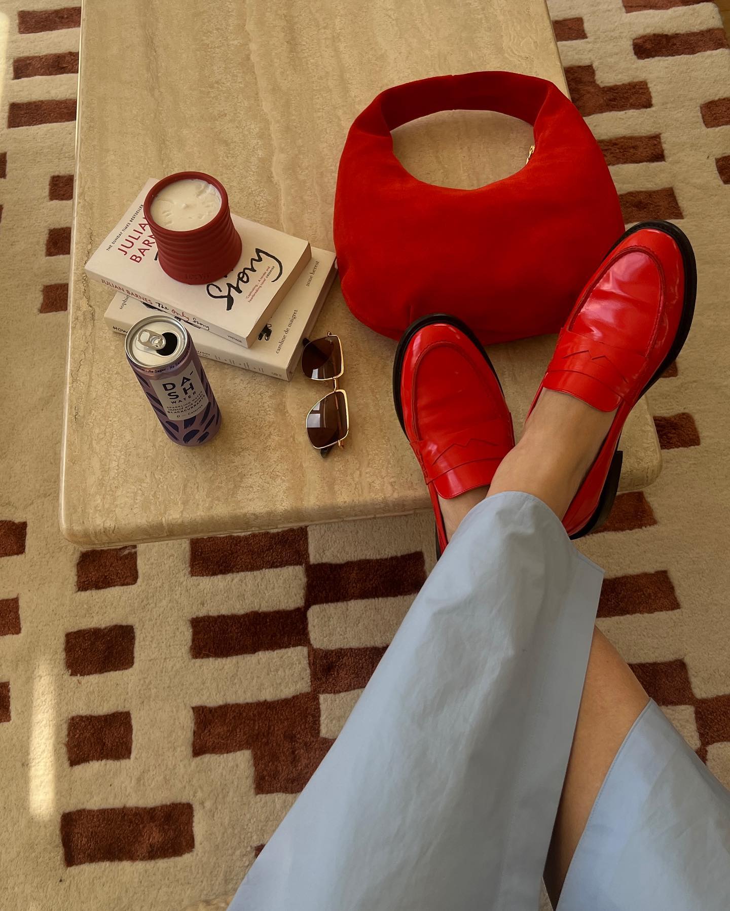 influencer Claudia Berresford poses with her feet propped up on a coffee table wearing a blue shirtdress and red patent loafers