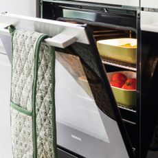 Close up of the built in oven with the door open and dishes on the oven shelves with tomatoes