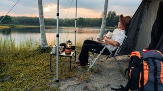 Woman sitting in camping chair outside tent next to lake