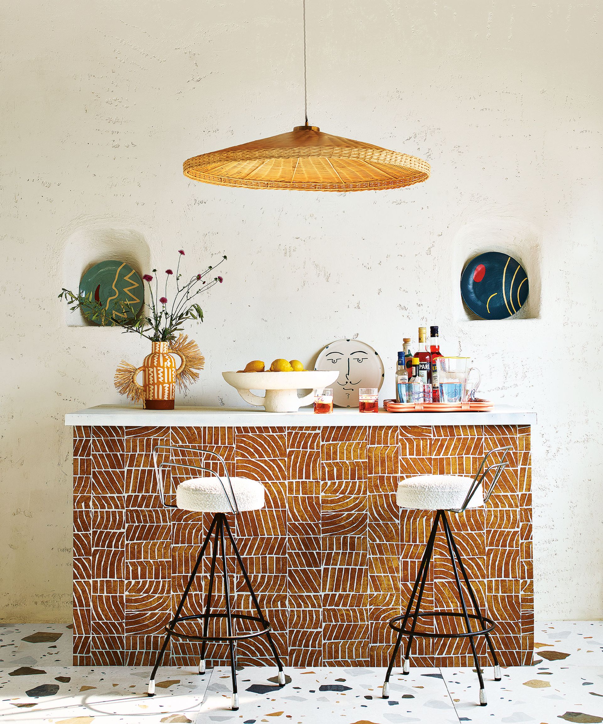Home bar with yellow patterned tiles, terrazzo floor tiles, low hanging natural pendant light, two arched alcove shelves f