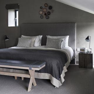 Grey bedroom with artwork on wall above bed, a grey upholstered headboard and a Scandi-style wooden bench at the end of the bed
